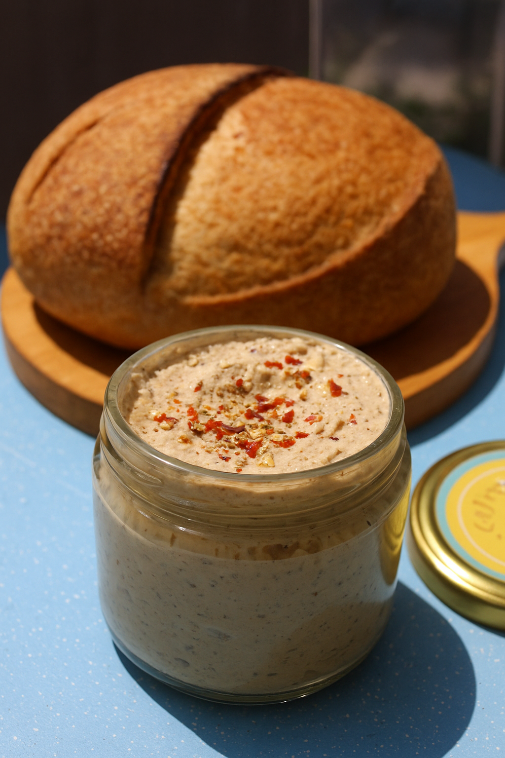Jar of spreadable food with a loaf of bread on a blue surface